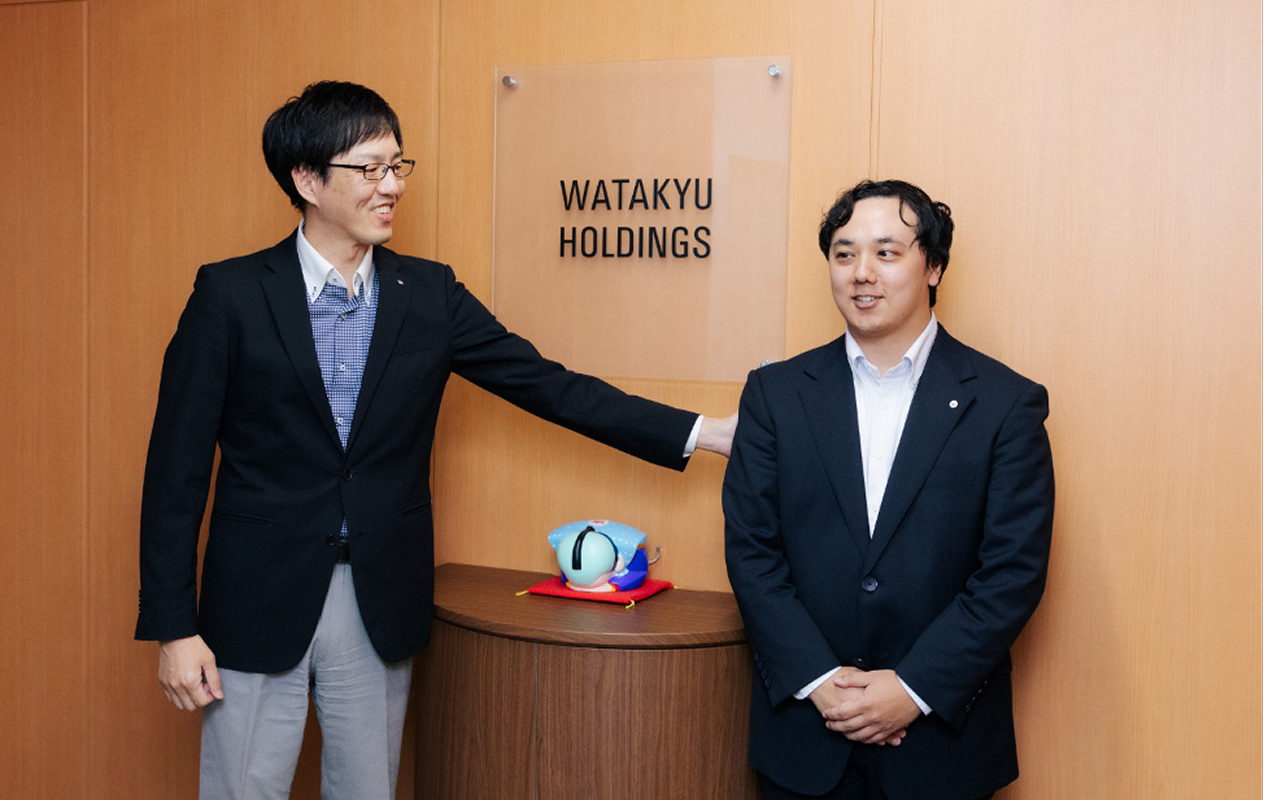 ワタキューホールディングスのエントランス前で笑顔で並ぶ両名